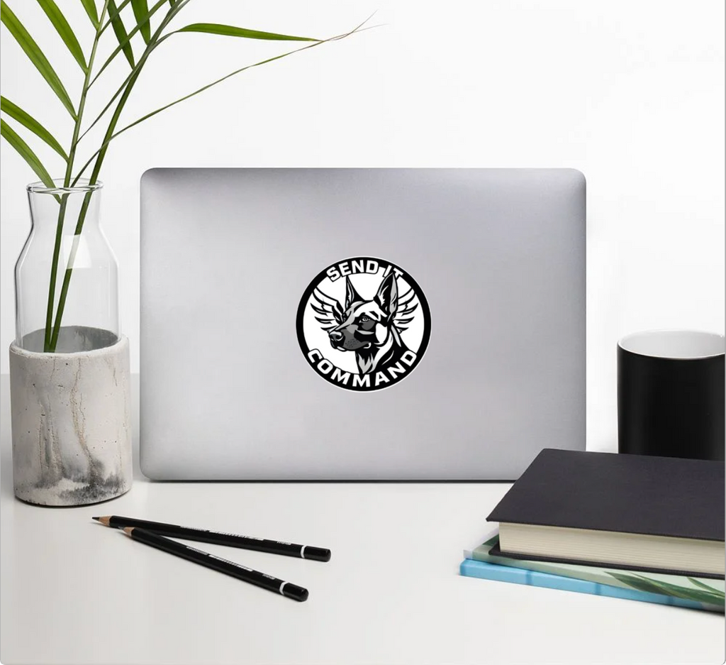 Durable SEND IT COMMAND sticker on a silver laptop with plants in the background, showcasing a bold design.